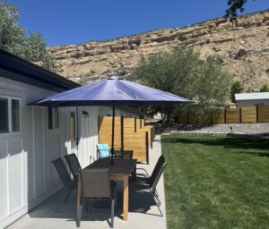 Homestead patio with dining table, chairs, and umbrella. Palisade views and green lawn. Outdoor living space.
