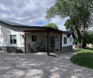 Homestead in Palisade, Colorado. White farmhouse with rocking chairs on the porch. Welcome sign. Metal roof.