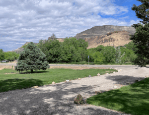 Scenic Palisade, Colorado vista. Green trees, grass, and a mountain backdrop under a cloudy sky. Outdoor landscape.