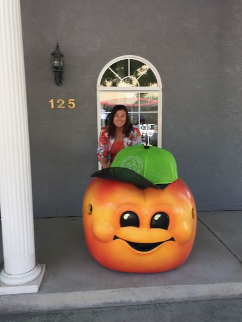Palisade Peach Festival mascot. Woman poses with a giant peach wearing a green hat. Palisade, Colorado.